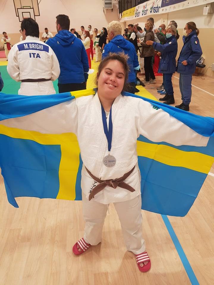 Amanda Orrbo i vit judodräkt med silvermedalj runt halsen. Håller upp en svensk stor flagga bakom ryggen.