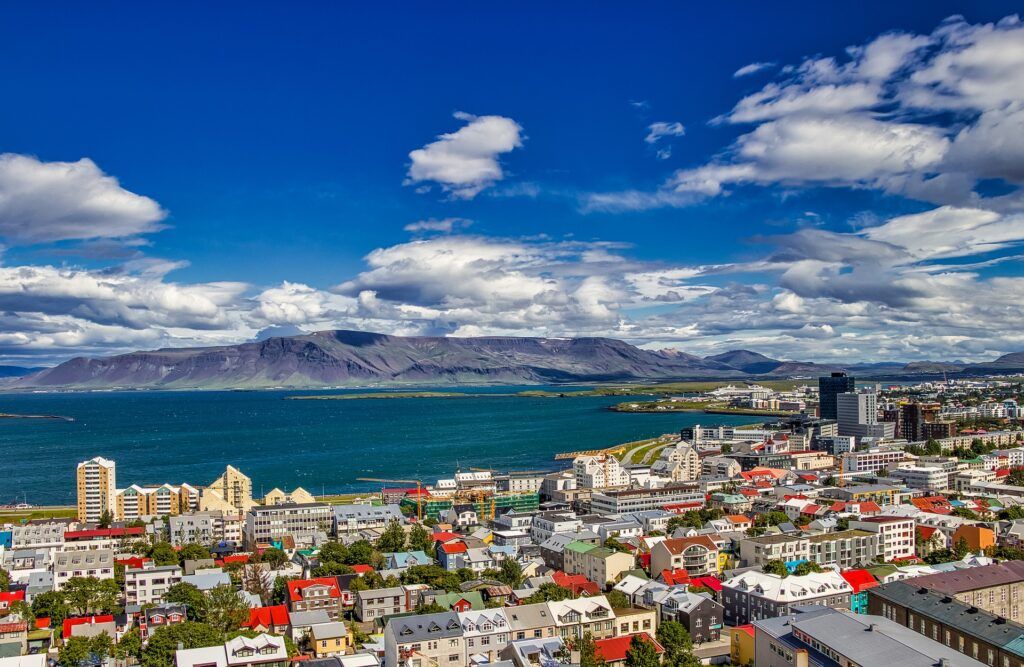 Bild över Reykjavik. Många hus i förgrunden, hav och berg i bakgrunden.