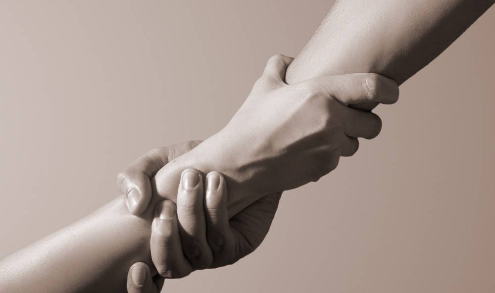 Två händer möts och håller varandra om handleden i en hjälpande gest.