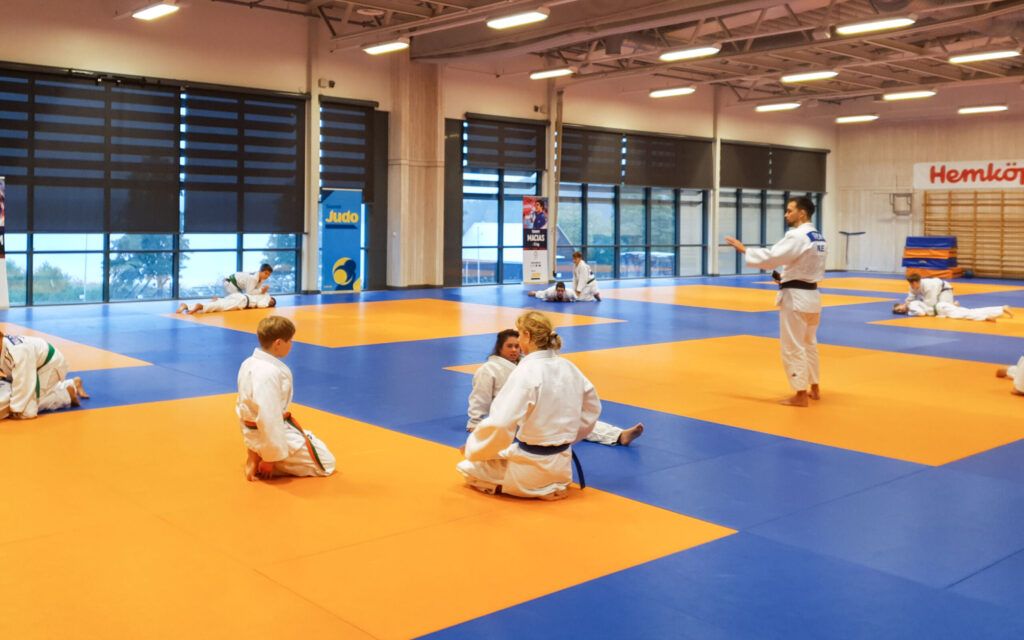 Barn sitter på judomattan och väntar på instruktioner från tränaren.