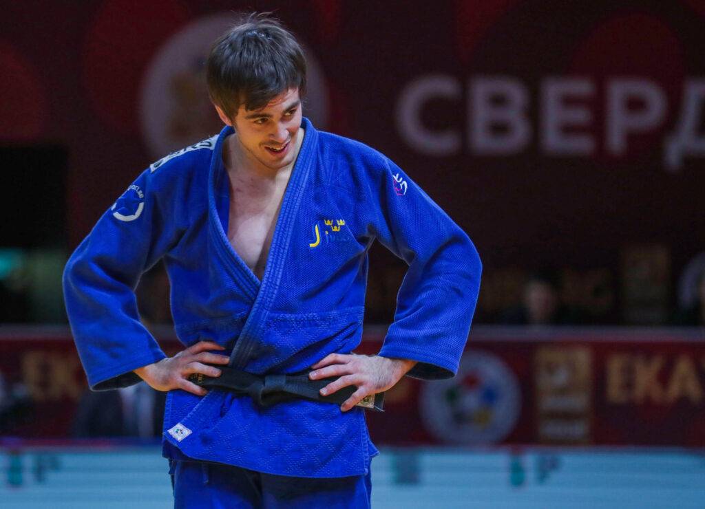 Tommy Macias i blå judodräkt står med armarna i sidan och tittar snett nedåt.