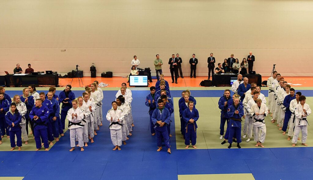 Tävlande står uppställda på judomattan i rader i sina lag.