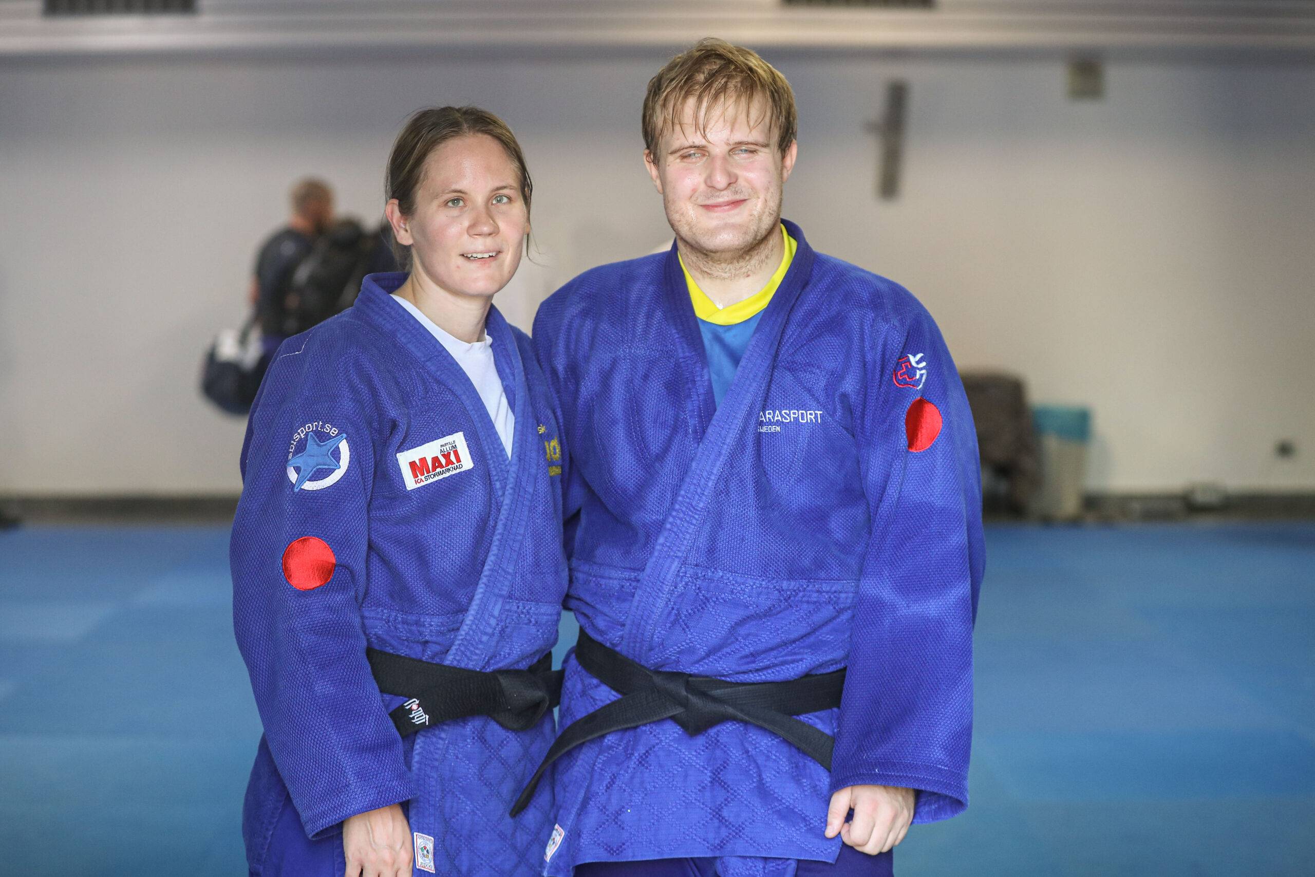 Nicolina Pernheim Goodrich och Oscar Widegren i blå judodräkter står bredvid varandra på träningsmattan.