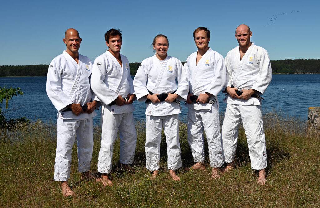 OS-truppen till Tokyo står i judodräkt utomhus framför vatten.
